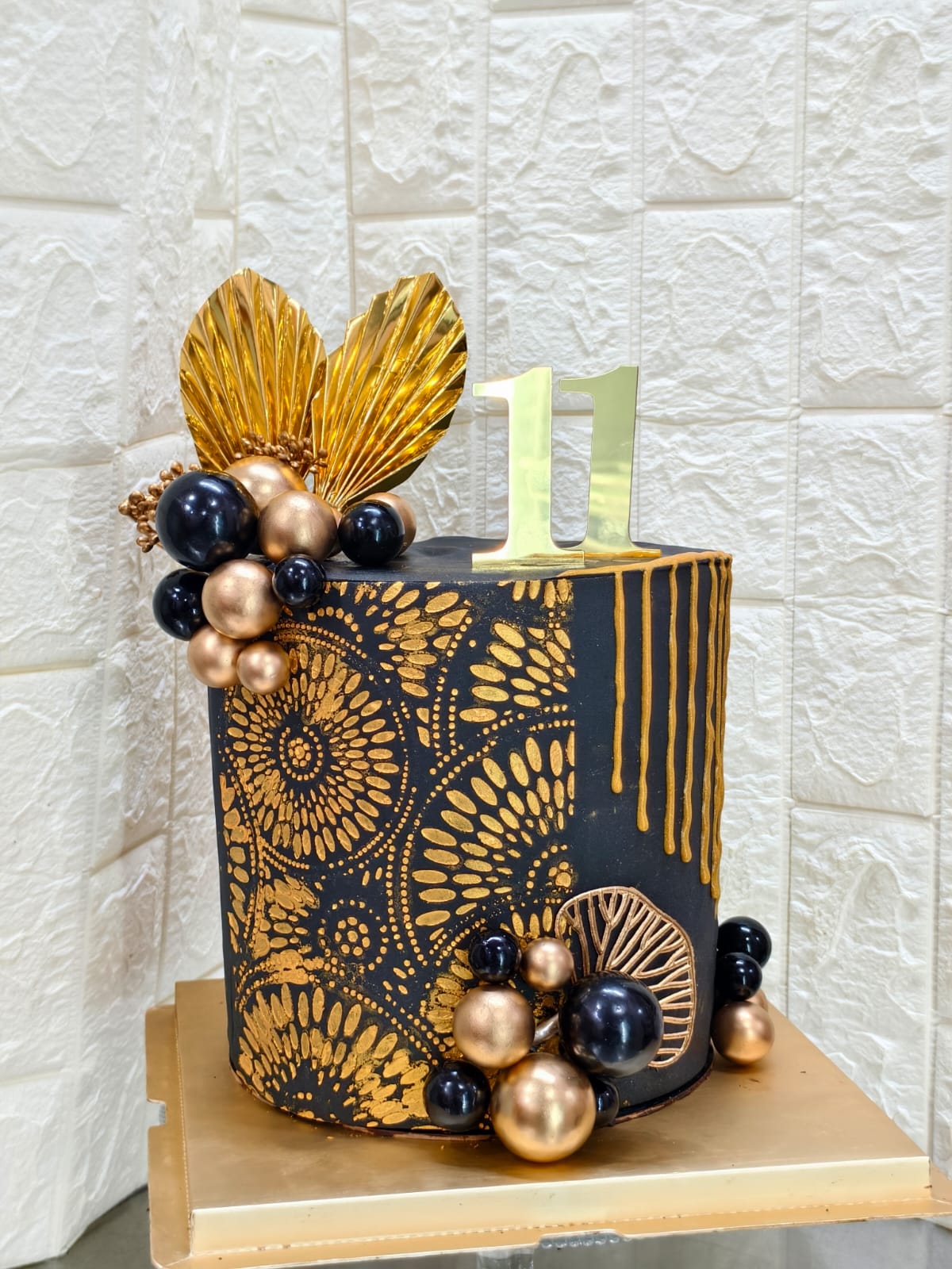 Black and gold celebration cake with metallic spheres, gold leaf accents and a number topper